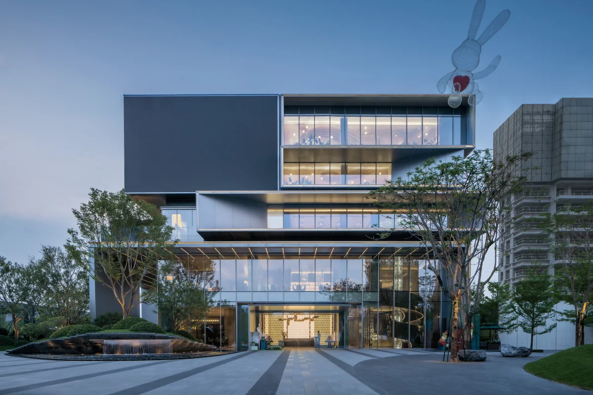 Completed modern city showroom in Foshan at dusk, with stick-built glass curtain wall, slim vertical aluminium mullions, a deep cantilevered upper volume, a large LED screen and a fountain in the foreground plaza
