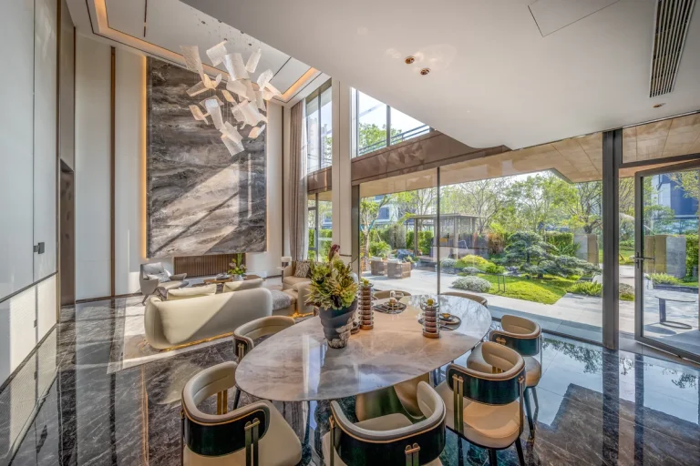 Interior of a high-end private villa in Chiang Mai Thailand with a floor-to-ceiling glass wall and a sliding door opening to a planted garden with mature trees and natural stone paving