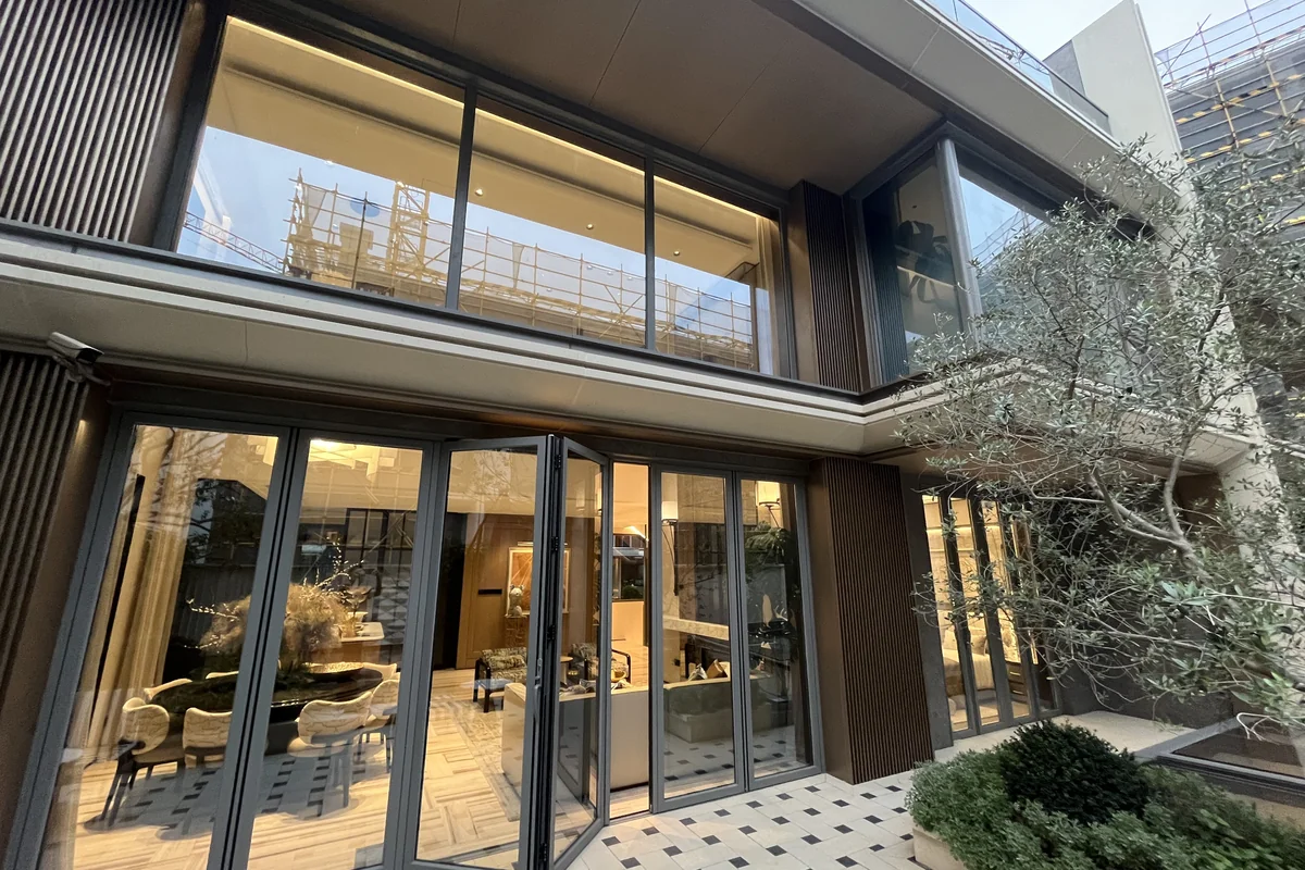 High-end private villa in Medan Indonesia at dusk, with a six-panel thermal-break aluminium folding glass door system opening from the principal living room to a stone-tiled patio and a planted olive tree