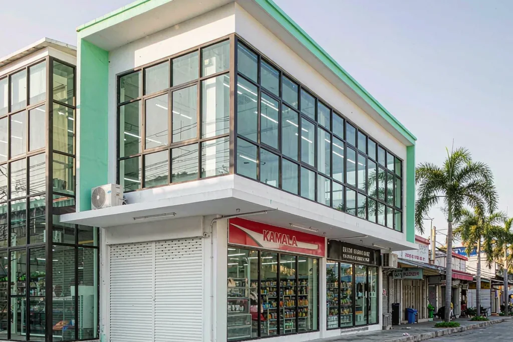 Renovated corner grocery store with a clean glazed corner facade and tropical planting