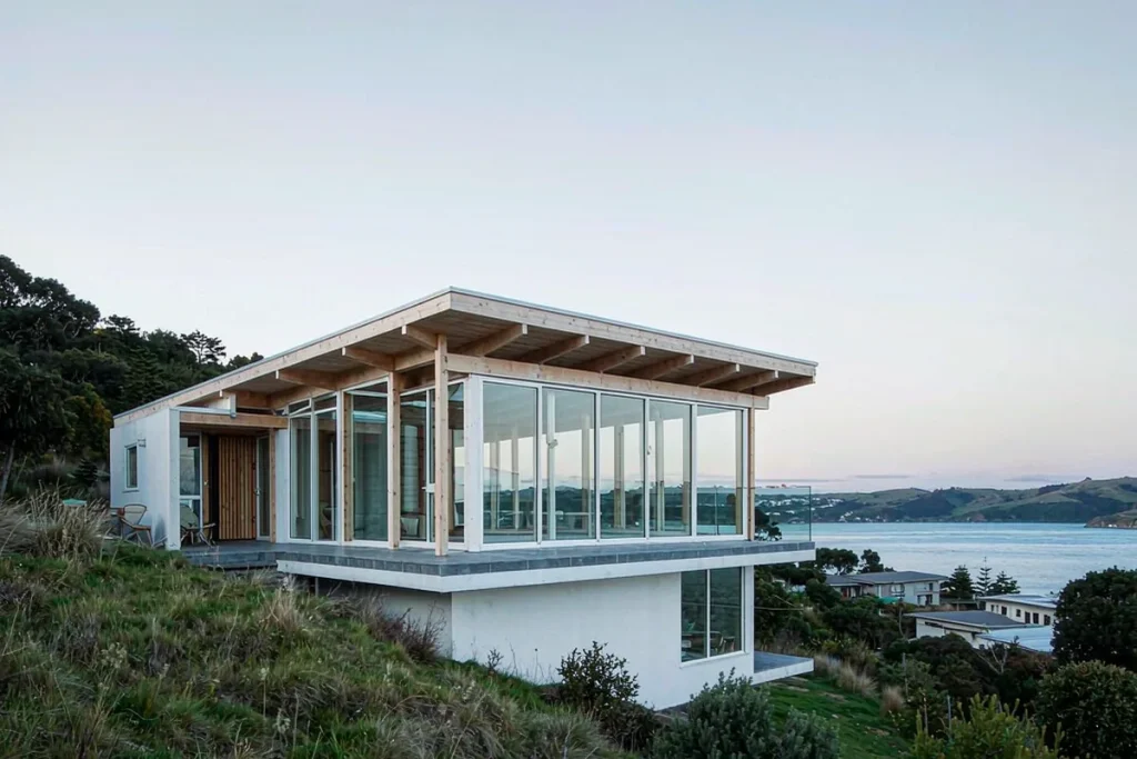 Two-storey coastal villa with frameless structural glazing wrapping the upper living level above a harbour