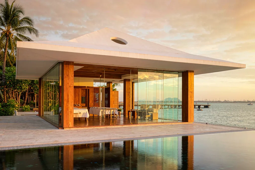 Single-storey waterfront spa pavilion with frameless glass walls opening to a calm sea view