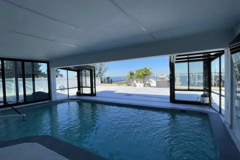 Indoor swimming pool in a private Long Island residence with large retractable glass walls opening to a marina view on a clear day