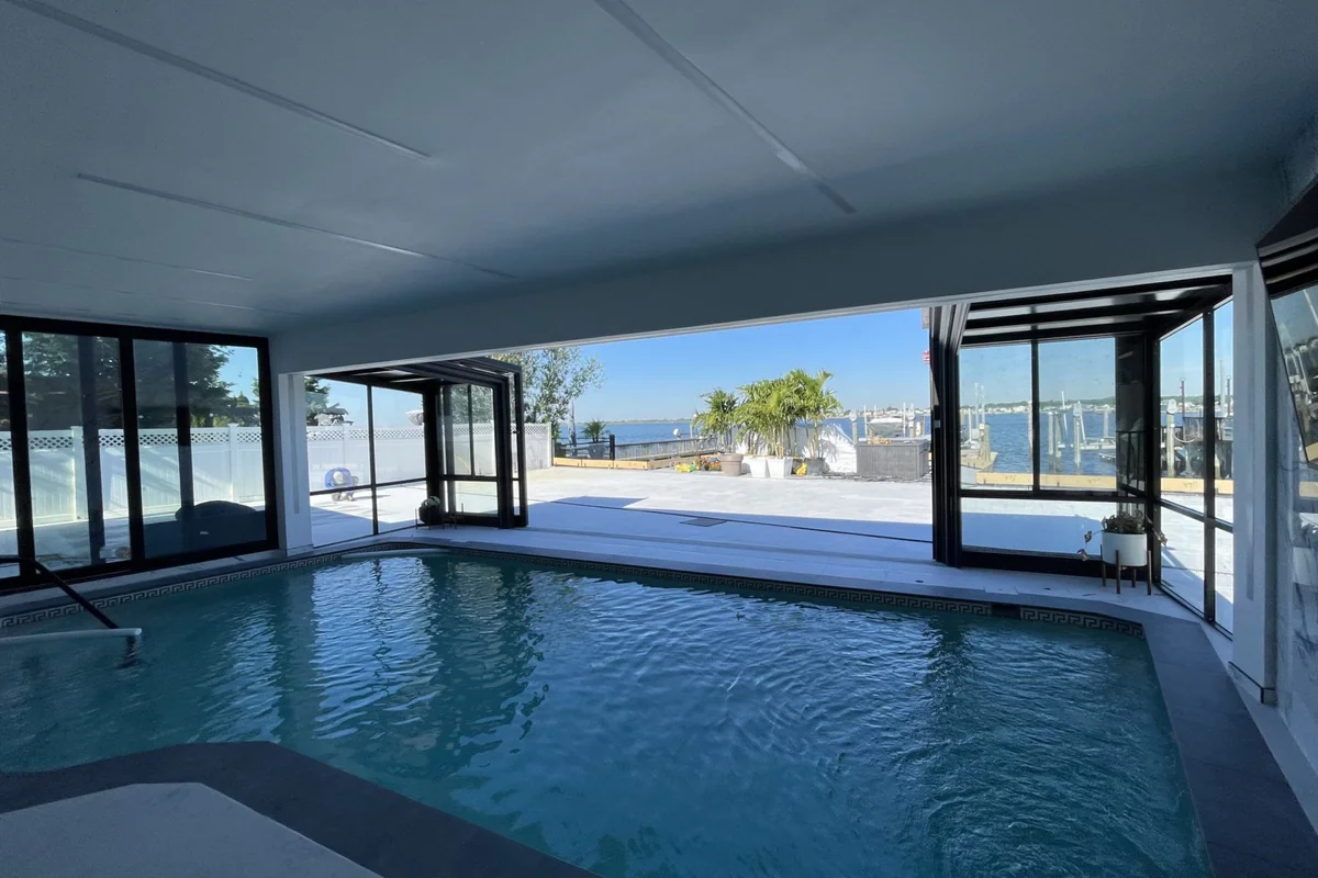 Indoor swimming pool in a private Long Island residence with large retractable glass walls opening to a marina view on a clear day